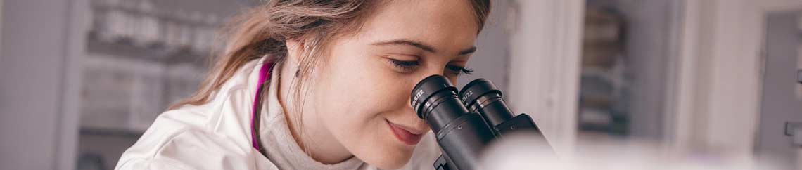 female in a lab coat looking down a microscope