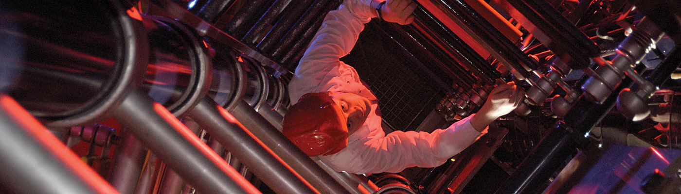 Man, illuminated by red light, climbing up a generator, peering upwards